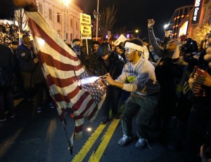 A protestor uses a lighter and an aerosol can to burn one of two American flags during a protest in the Chinatown area of Washington, Tuesday, Nov. 25, 2014. A grand jury in Ferguson, Mo., on Monday, Nov. 24th, 2014, declined to indict police officer Darren Wilson in the shooting death of Michael Brown, an unarmed African-American man. (AP Photo/Alex Brandon)